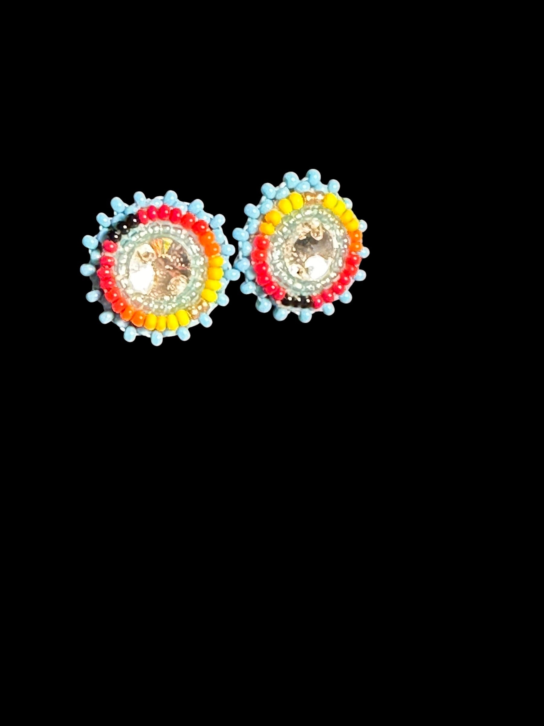 A pair of colorful beaded stud earrings with circular designs featuring red, yellow, and light blue beads surrounding a central clear stone, set against a solid black background.